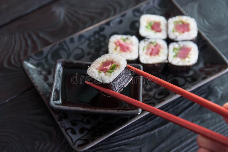 Hand using chopsticks pick. Maki-Sushi, tuna-maki rolls on a black stone plate. Fresh made Sushi set with tuna, cheese and cucumbe