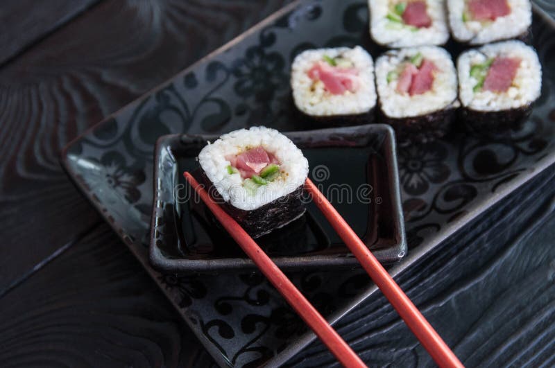 Hand using chopsticks pick. Maki-Sushi, tuna-maki rolls on a black stone plate. Fresh made Sushi set with tuna, cheese and cucumbe