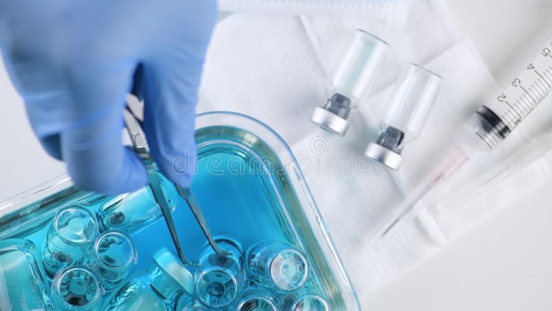 Hand van de wetenschapper gebruikt de arts een tang of pincet met een ampul om in blauw alcohol op glaswerk in het laboratorium va