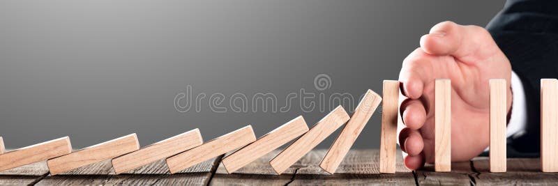 Hand Of Businessman Blocking Domino Effect On Wooden Table - Investment Protection And Security Concept. Hand Of Businessman Blocking Domino Effect On Wooden Table - Investment Protection And Security Concept