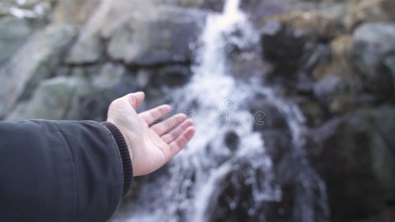 Hand vor einem kleinen Wasserfall in einem Wald