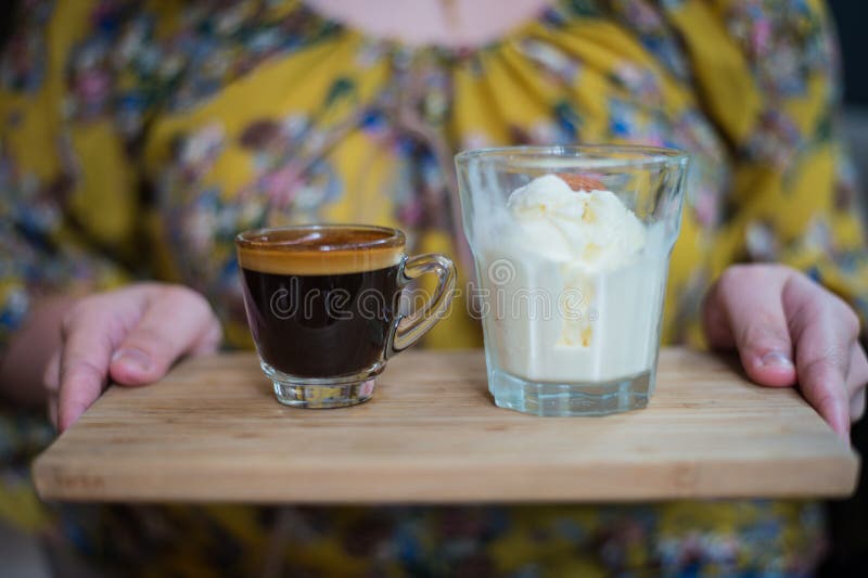 Hand of woman holding a cup of Affogato coffee or espresso with icecream on Wooden board