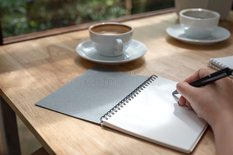 A hand writing down on a white blank notebook with coffee cup on wooden table royalty free stock images A hand writing down on a white blank notebook with coffee cup on wooden table royalty free stock images