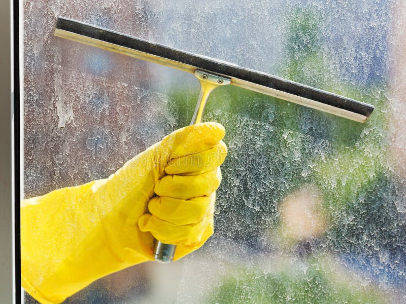 Hand in yellow glove washes window by squeegee royalty free stock image