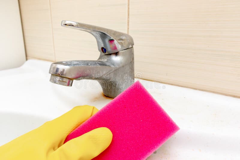 Hand in yellow rubber gloves holding a sponge for washing dirty faucet with limescale, calcified water tap with lime scale on stock photography Hand in yellow rubber gloves holding a sponge for washing dirty faucet with limescale, calcified water tap with lime scale on stock photography