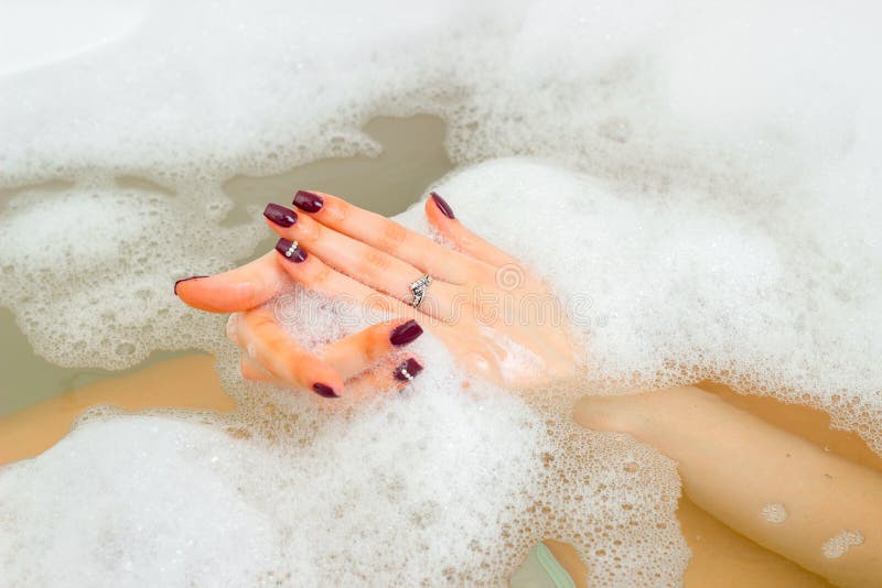 The hand of a young girl in the water with foam in bathtub