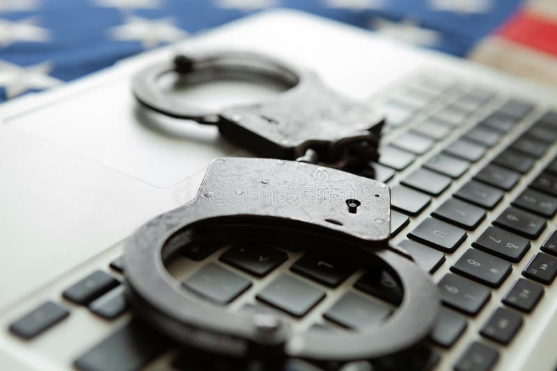Handcuffs over a laptop with an old USA flag on background - close up studio shot stock images Handcuffs over a laptop with an old USA flag on background - close up studio shot stock images