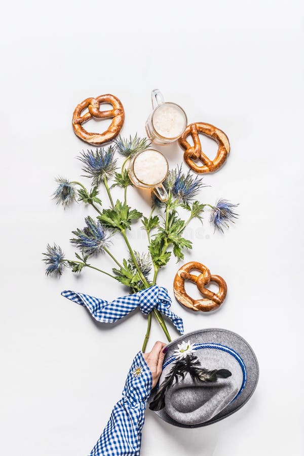 Handduk av kvinnor i traditionell blå skjorta som håller hinna av alpina blommor på vit bakgrund med påssjuka och muggar av öl, ö royaltyfri bild Handduk av kvinnor i traditionell blå skjorta som håller hinna av alpina blommor på vit bakgrund med påssjuka och muggar av öl, ö royaltyfri bild