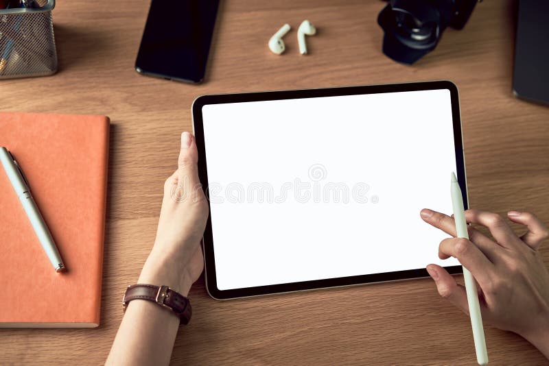 Handen die tablet gebruiken met een leeg scherm en digitale pen vasthouden, smartphone met camera en accessoires op houttafel stock afbeelding Handen die tablet gebruiken met een leeg scherm en digitale pen vasthouden, smartphone met camera en accessoires op houttafel stock afbeelding