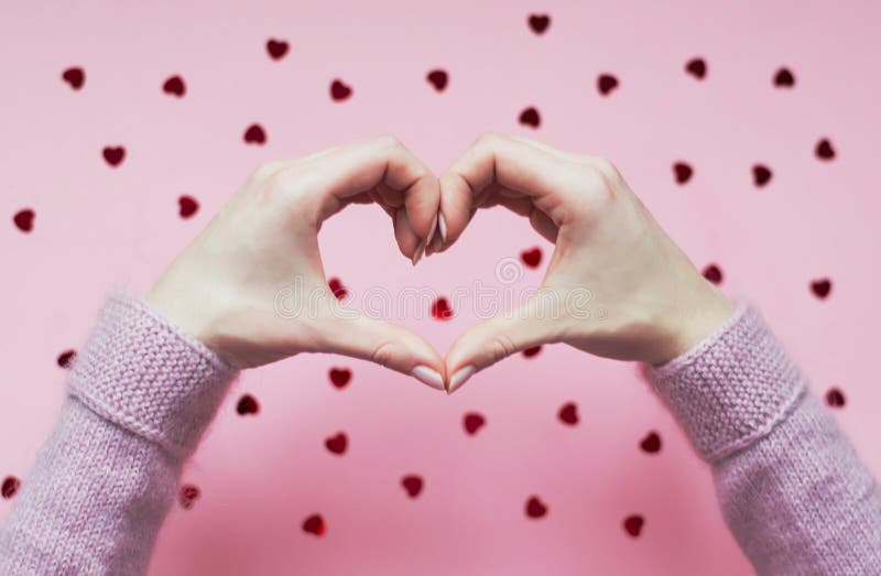 Handen gevouwen hart op roze achtergrond met rode harten stock fotografie Handen gevouwen hart op roze achtergrond met rode harten stock fotografie