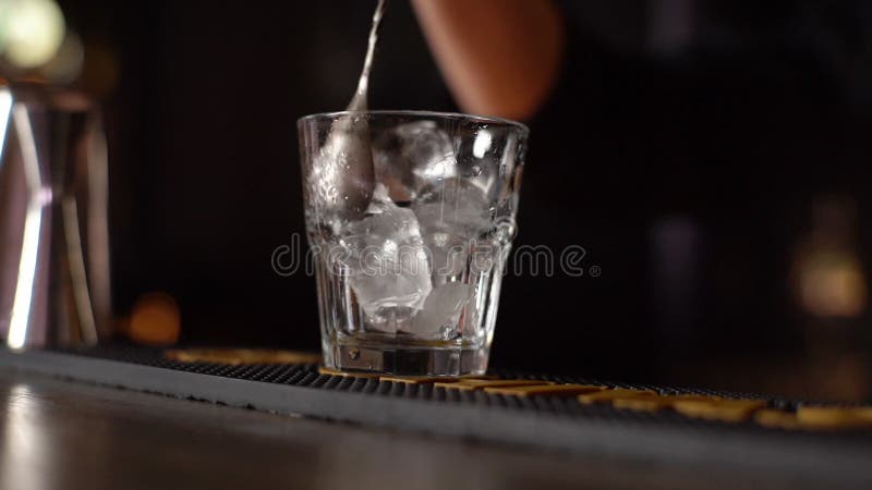 Handen van de stolling van onherkenbaar barman die roerend ijs in glas roteert met een lepel op de staafbank.