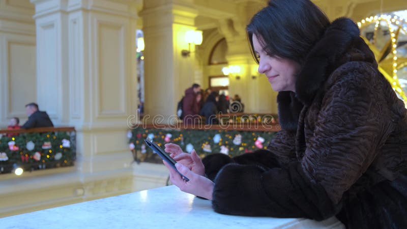 Handen van een vrouw van middelbare leeftijd brunette drukt op een smartphone in een winkelcentrum