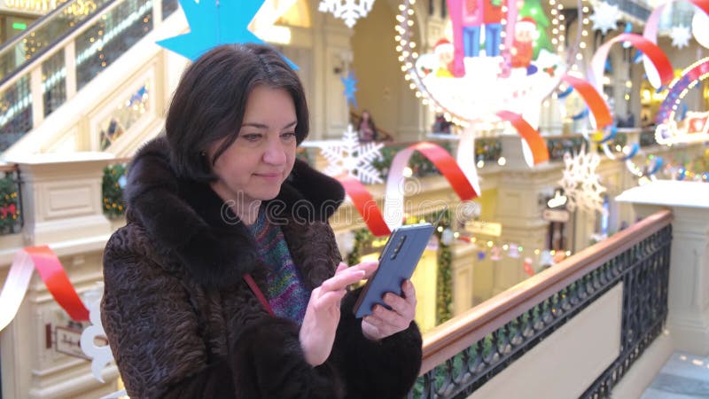Handen van een vrouw van middelbare leeftijd brunette drukt op een smartphone in een winkelcentrum