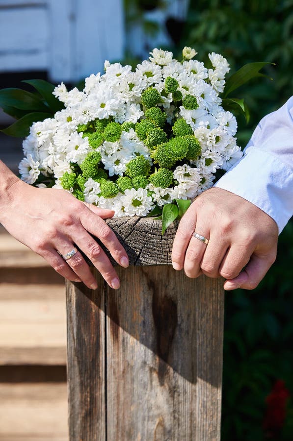 Handen van onlangs echtpaar die naast huwelijksboeket van wit decoratief madeliefje op natuurlijke oude houten plank liggen stock foto's Handen van onlangs echtpaar die naast huwelijksboeket van wit decoratief madeliefje op natuurlijke oude houten plank liggen stock foto's