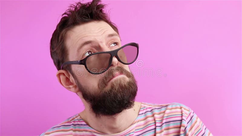 Handige bebaard man in zonnebril die op een roze achtergrond kijkt