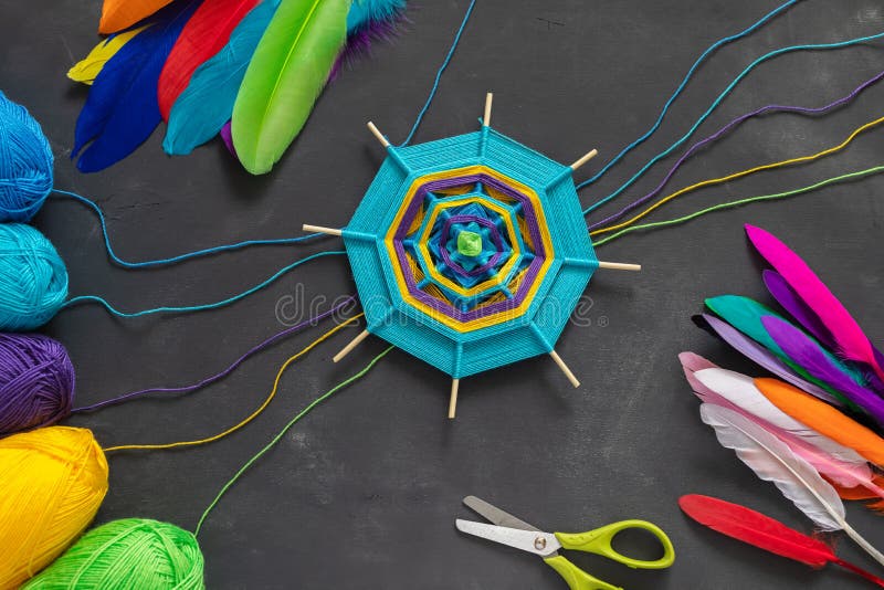 Colored handmade mandala and multicolored feathers on grey background. Handmade mandala of multicolor blue, purple, yellow yarn threads and multicolored stock image Colored handmade mandala and multicolored feathers on grey background. Handmade mandala of multicolor blue, purple, yellow yarn threads and multicolored stock image