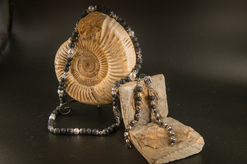 Handmade necklace and earrings made of silver and volcanic stone on ammonite and trilobite on black royalty free stock photo