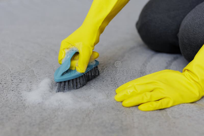 Handnah in gelben Gummihandschuhen, Teppich mit Bürste und Schaum reinigen