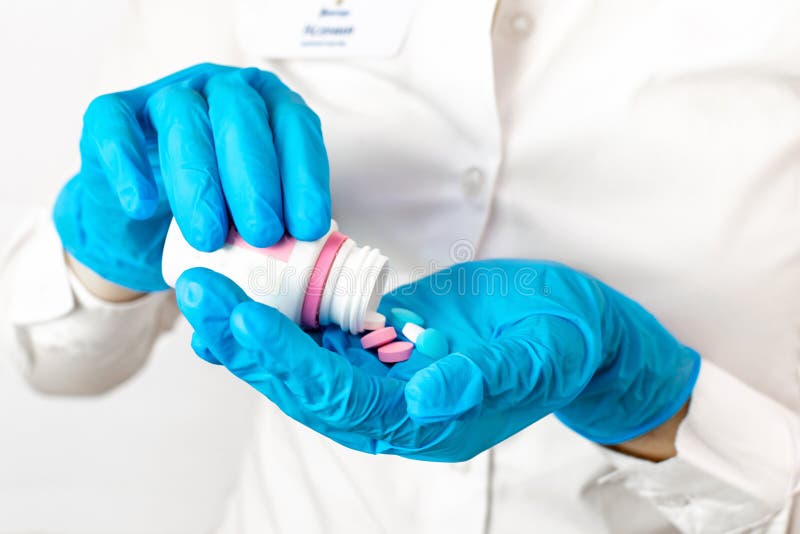 Hands in blue medical gloves holding a bottle with multi-colored pills close-up. The doctor gives a dose of medication, vitamins