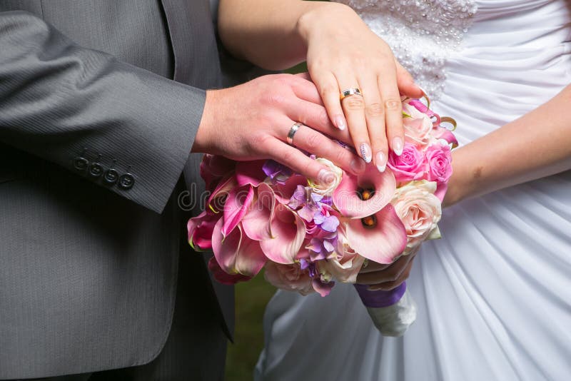 Hands of bride and groom on wedding bouquet