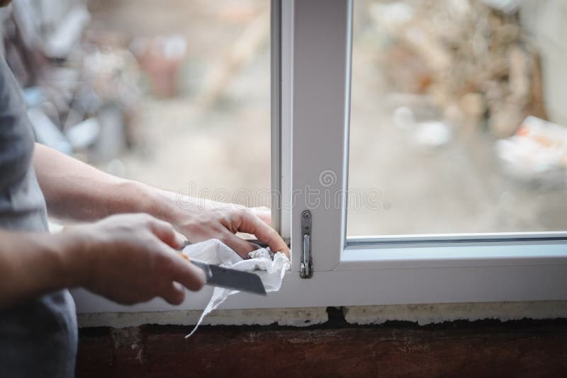 A caucasian man washing his hands with a dry paper napkin using a construction knife inside a window frame opening, close-up side view with selective focus. The concept of home renovation, washing window frames. A caucasian man washing his hands with a dry paper napkin using a construction knife inside a window frame opening, close-up side view with selective focus. The concept of home renovation, washing window frames.