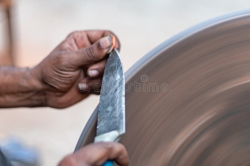 Hands of Construction Worker Sharpens a Knife on Sanding Machine Stock