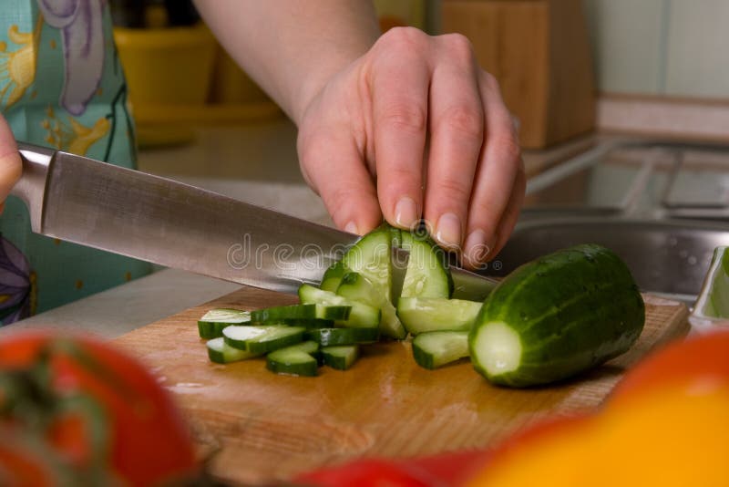 Hands of cook cutting cucumber.