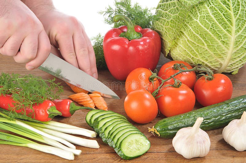 Hands cut a knife a carrot among vegetables