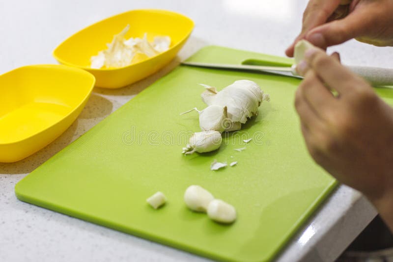 Hands are Cutting Fresh Garlic on a Green Board in the Kitchen Stock