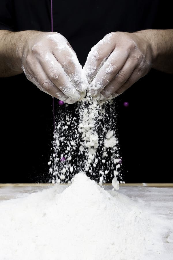 The chef hands are dropping flour over a wooden table. The chef hands are dropping flour over a wooden table