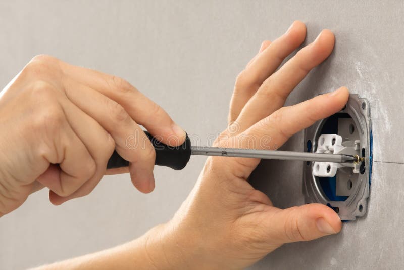 Hands of Electrician Installing Light Switch with Screwdriver Stock