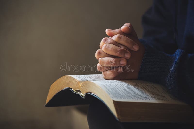 Hands folded in prayer on a Holy Bible in church concept for faith