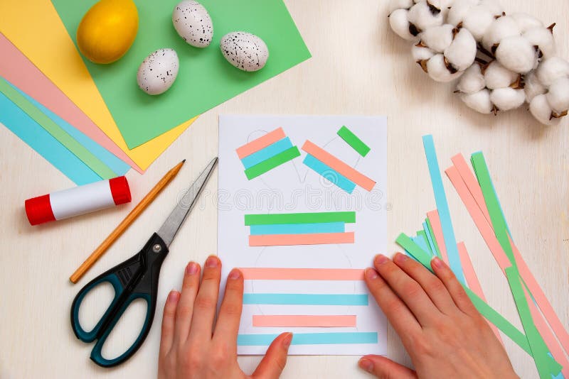Hands are gluing strips of paper, colored sheets, scissors, glue, Easter eggs on a light table. DIY concept. Step by step stock photo