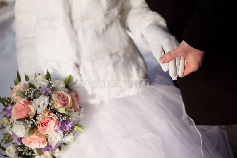 Hands of groom and bride with wedding bouquet