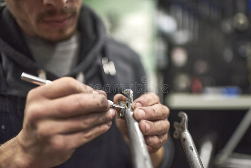 Hands of an Hispanic Man Removing Paint Residue from a Bike Frame Stock