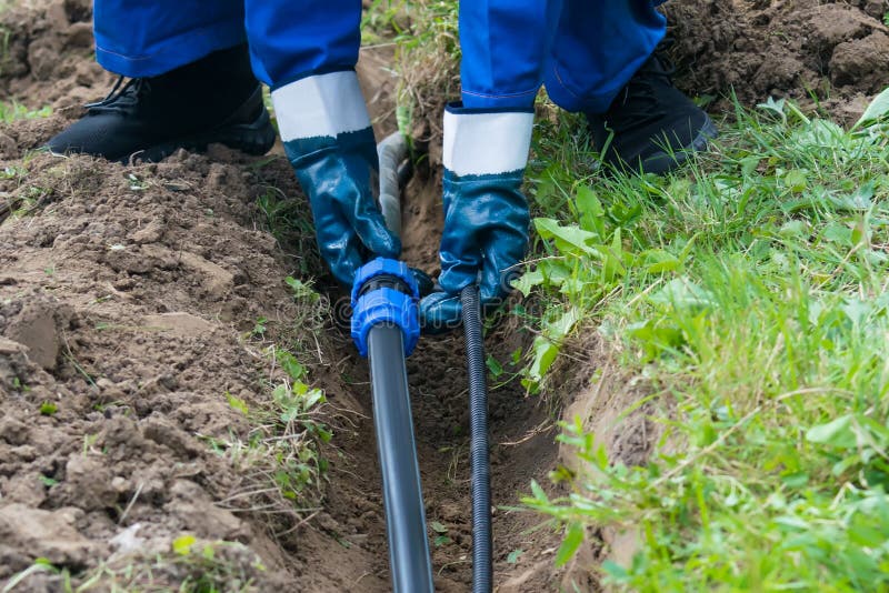 Hands Hold a Black Pipe Over a Dug Hole in the Ground Stock Photo