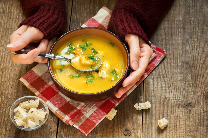 Hands hold bowl of vegetable soup. Woman hands holding bowl of vegetable soup with parsley and croutons over wooden background - healthy winter vegetarian food stock photography Hands hold bowl of vegetable soup. Woman hands holding bowl of vegetable soup with parsley and croutons over wooden background - healthy winter vegetarian food stock photography