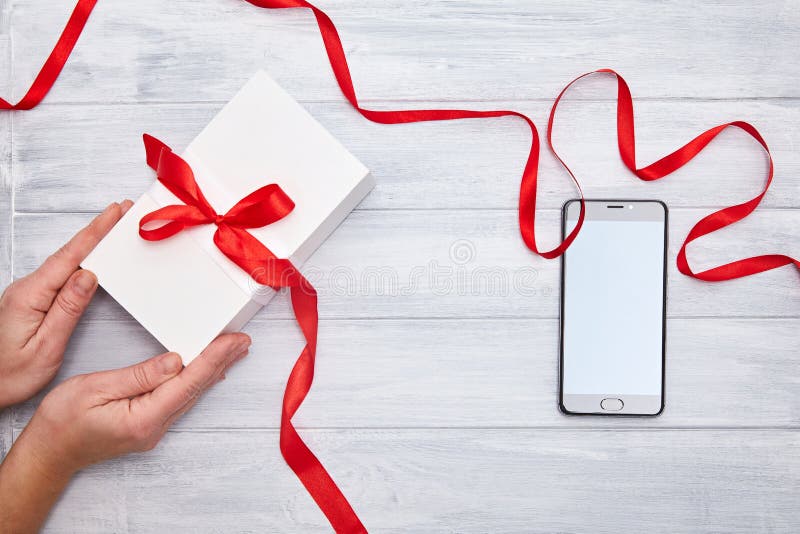 Hands hold Gift Box with red ribbon and smartphone on a woodem background royalty free stock photography Hands hold Gift Box with red ribbon and smartphone on a woodem background royalty free stock photography