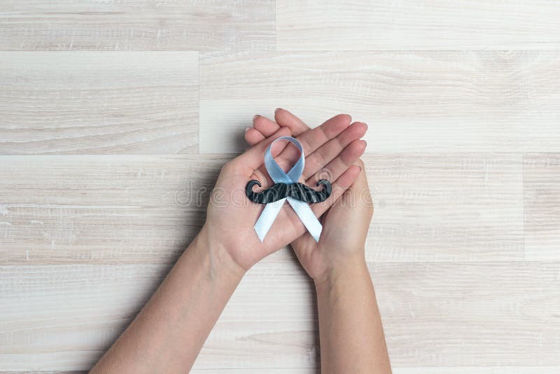 Hands holding a blue ribbon with mustache on wooden table. Prostate cancer awareness royalty free stock images Hands holding a blue ribbon with mustache on wooden table. Prostate cancer awareness royalty free stock images