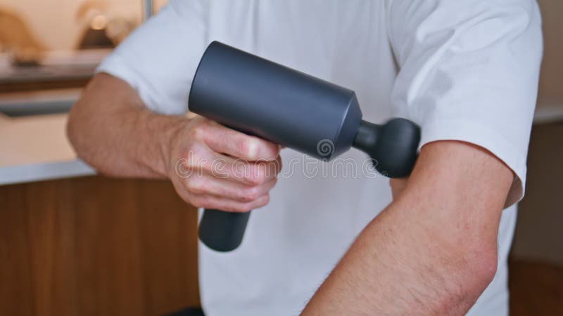 Hands holding massage gun relieving arm muscles pain in home kitchen closeup. stock video
