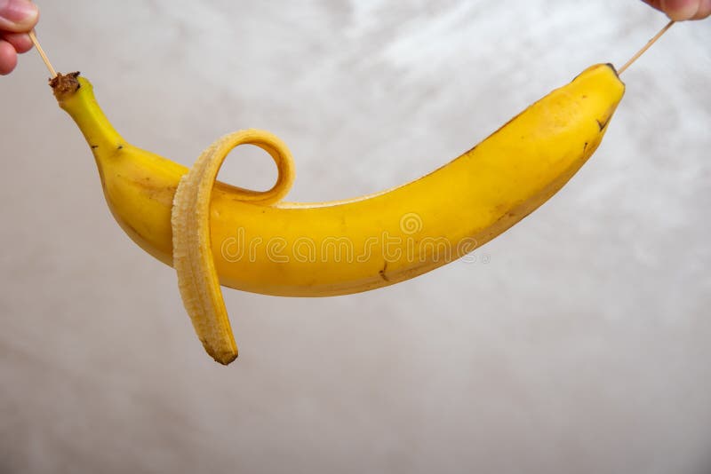 Hands Holding Peeled Banana By Wooden Sticks Close Up Over Gray