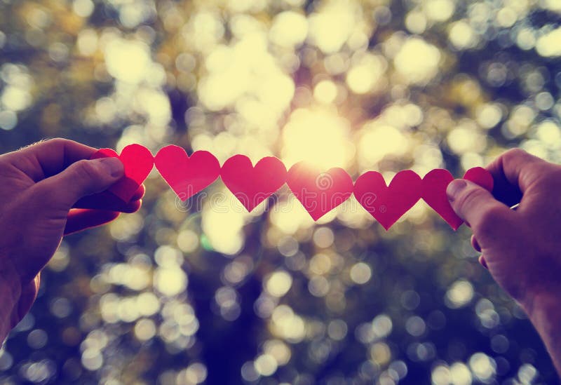 Hands holding a string of paper hearts up to the sun during sunset