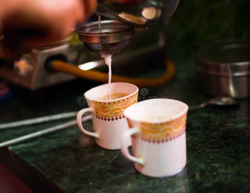 An Indian Woman Using a Tea Strainer for Pouring Tea Over a Cup at Home