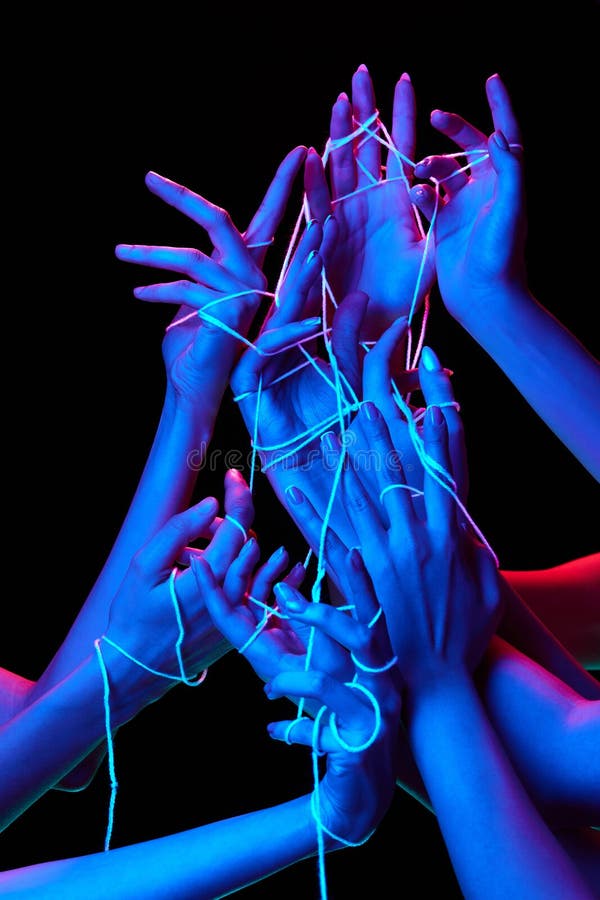 Hands interact with luminescent threads in multicolored neon lighting against black studio background, symbolizing stock photo