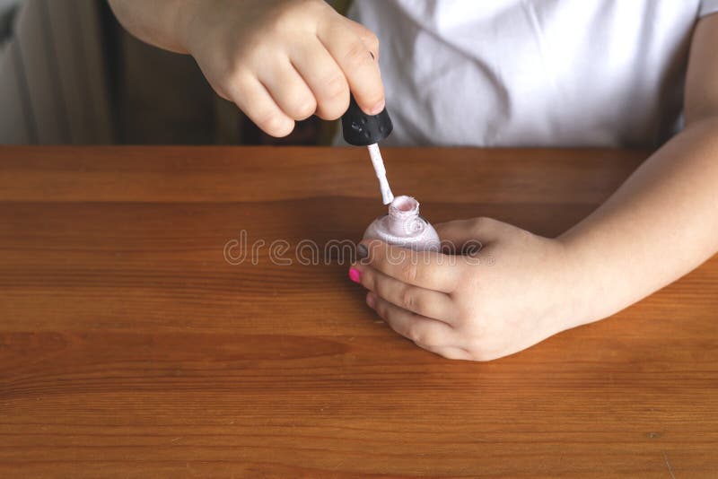 Hands of a little girl who paints her nails with nail polish behind a wooden stall. Hands of a little girl who paints her nails with nail polish behind a wooden stall