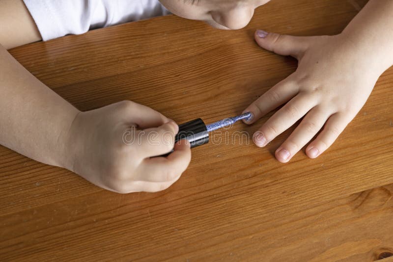 Hands of a little girl who paints her nails with nail polish behind a wooden stall