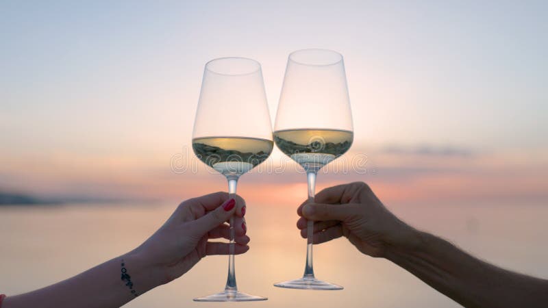 Hands making cheers with wine in glass against the sea