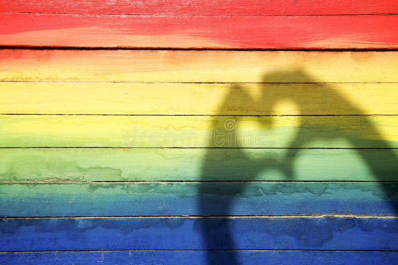 Hands making love heart shadow on rainbow colors painted on slats of weathered wood. Hands making love heart shadow on rainbow colors painted on slats of weathered wood