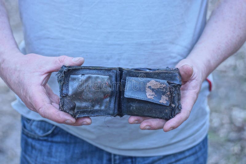 Hands of a man in gray clothes holding an old open black leather wallet. On the street