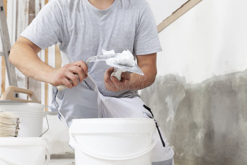 Hands man plasterer construction worker at work closeup, takes plaster from bucket and puts it on trowel to plaster the wall